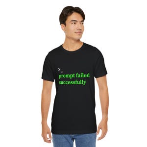 Op de afbeelding: Zwart T-shirt met de tekst "prompt failed successfully" in het groen. De tekst wordt weergegeven in een terminal-achtige lettertype. Het shirt heeft een ronde hals.