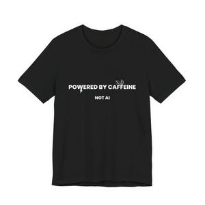 Puede incluir: Camiseta negra con texto blanco "POWERED BY CAFFEINE" con un rayo gráfico, y "NOT AI" debajo. La camiseta es de manga corta y cuello redondo.