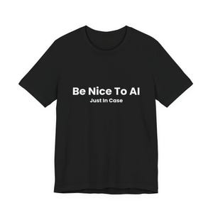 Op de afbeelding: Zwart t-shirt met de witte tekst "Be Nice To AI" boven "Just In Case". Het shirt met korte mouwen is gemaakt van een zacht materiaal en is geschikt voor vrijetijdskleding.