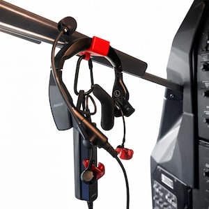 May include: Black aviation headset with red accents, hanging from a metal bar. The headset includes a microphone, ear pieces, and a control unit. The image is set against a white background.