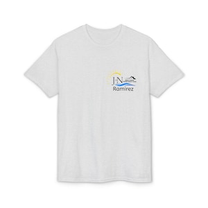 Peut inclure: T-shirt gris clair à col rond. Le t-shirt présente un petit logo sur la poitrine gauche avec le texte "JN Ramirez Brothers Construction". Le logo comprend un soleil, de l'eau et une maison.