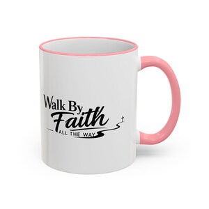 Puede incluir: Taza de cerámica blanca con asa y borde rosas. La taza presenta el texto "Walk By Faith All The Way" en escritura negra. Una pequeña cruz es visible cerca del final del texto.