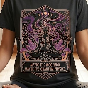May include: Dark gray t-shirt featuring a graphic design with a woman meditating, surrounded by celestial elements and crystals. The text reads "MAYBE IT'S WOO-WOO. MAYBE IT'S QUANTUM PHYSICS." The shirt is worn during a yoga session.