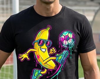 May include: Black t-shirt with a cartoon banana wearing sunglasses and kicking a football. The banana is yellow with colourful accents, and the football is black and white. A person is holding a football.