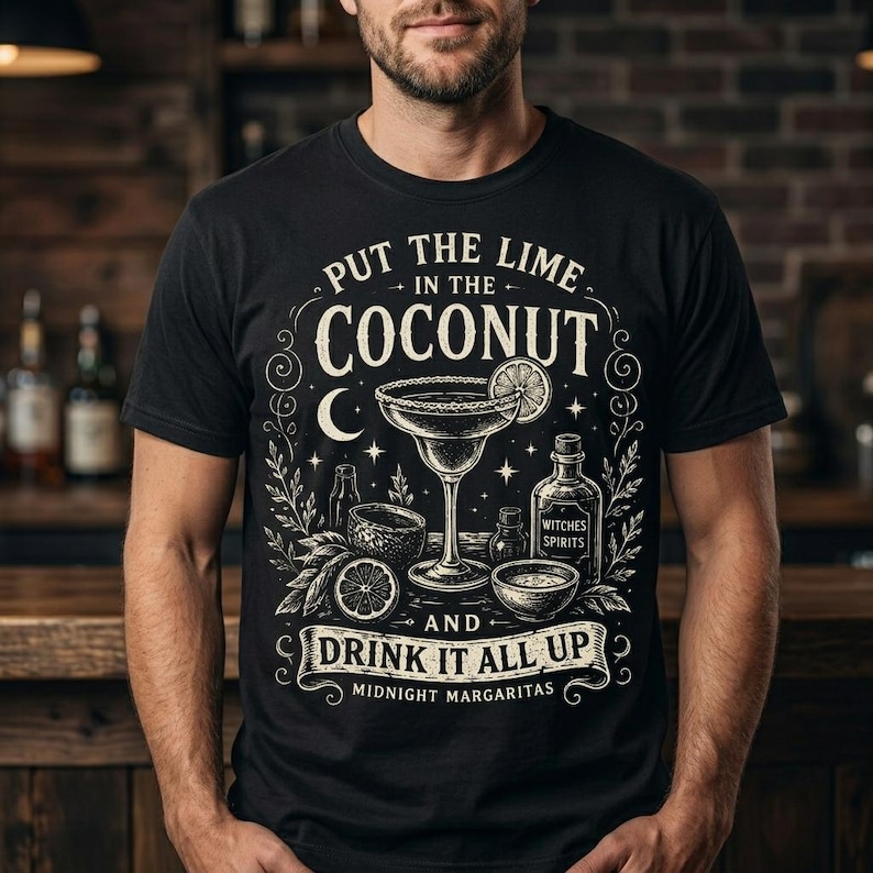 May include: A black t-shirt featuring a white graphic illustration of a margarita glass, a lime slice, and bottles. The text reads: PUT THE LIME IN THE COCONUT AND DRINK IT ALL UP MIDNIGHT MARGARITAS. The design includes stars, a crescent moon, and leaves.