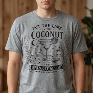 May include: A heather grey t-shirt featuring a black graphic print of a margarita glass, a lime slice, and a bottle labelled Witches Spirits. The text reads Put the Lime in the Coconut and Drink it all up, with Midnight Margaritas at the bottom.