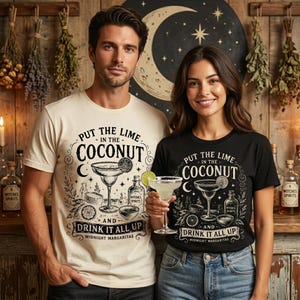 May include: A cream-coloured t-shirt and a black t-shirt, both featuring a graphic print of a margarita glass, a lime slice, and the text "PUT THE LIME IN THE COCONUT AND DRINK IT ALL UP MIDNIGHT MARGARITAS" in a decorative black font.
