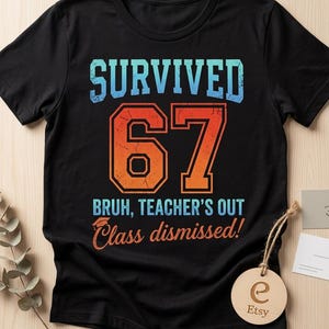 Könnte beinhalten: Schwarzes T-Shirt mit dem Text "SURVIVED 67 BRUH, TEACHER'S OUT Class dismissed!" in Blau und Orange. Ein Holzanhänger mit dem Etsy-Logo hängt am Shirt. Das Shirt ist ein Freizeitartikel.
