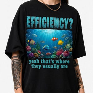 May include: A black short-sleeve t-shirt featuring a graphic of an underwater coral reef scene with various colourful fish. The text EFFICIENCY? is printed in light blue above the scene, and yeah that's where they usually are is below.