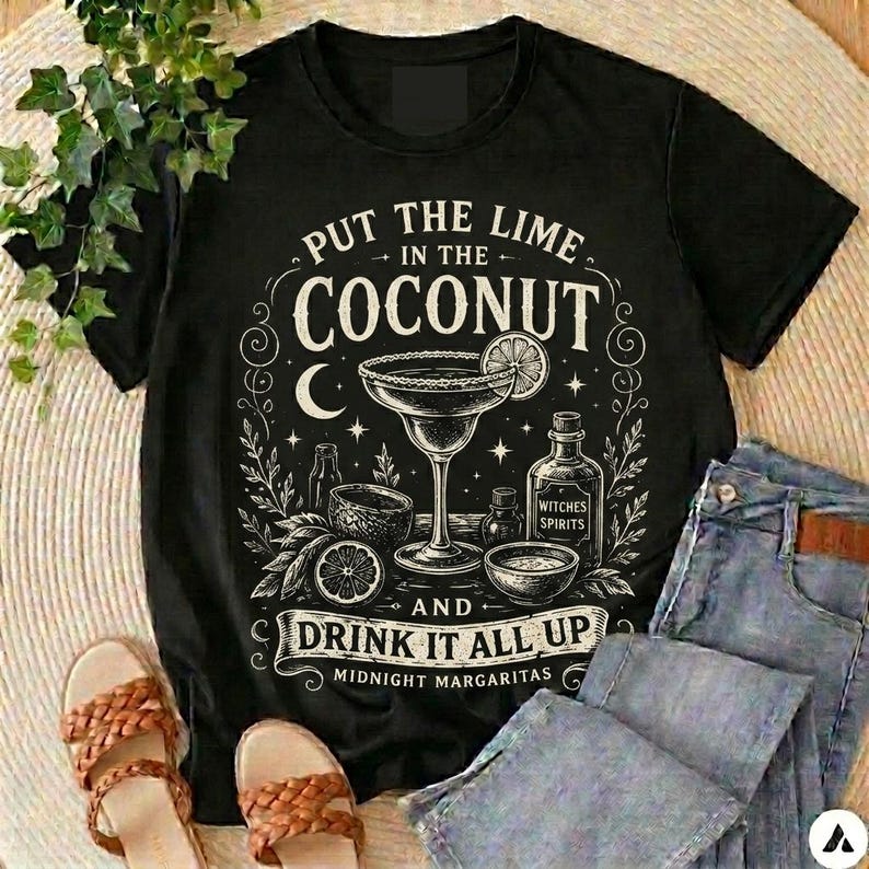 May include: A black short-sleeved t-shirt featuring a white graphic print of a margarita glass, a bottle labelled Witches Spirits, and the text Put the lime in the coconut and drink it all up Midnight Margaritas with stars and moon accents.