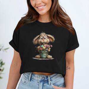 May include: Black t-shirt with a cartoon bunny wearing glasses and holding a bucket of flowers and Easter eggs. The bunny has tan fur and is smiling. The bucket is light blue and filled with colourful flowers and eggs.