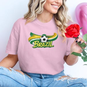 Woman in pink shirt with Brazil soccer logo holding a red rose.