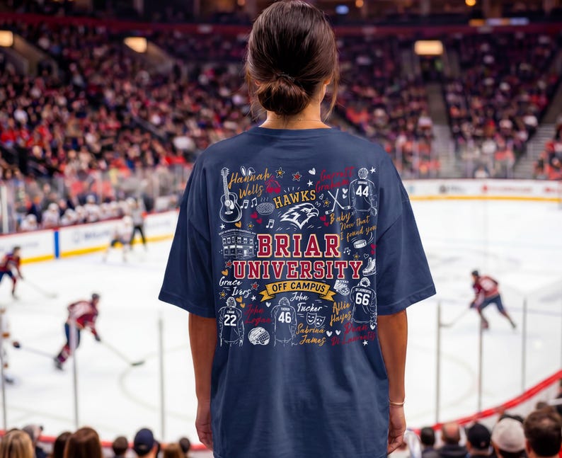 May include: A navy blue t-shirt featuring a graphic print on the back with the text Briar University Off Campus, surrounded by illustrations of hockey jerseys, a guitar, a building, and various names written in a decorative script font.