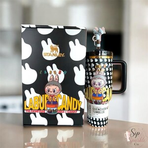 May include: A black and white Stanley Labubu The Monsters hard candy tumbler with a matching box. The tumbler features a character graphic, a black handle, and a lid with a small character topper. The box displays the Stanley logo and Labubu text.