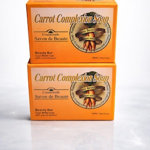 Pode incluir: Duas caixas laranja de "Carrot Complexion Soap" empilhadas. Cada caixa apresenta o nome do produto, uma ilustração de cenoura e as palavras "Countryside Savon de Beaute". As caixas são rotuladas como uma barra de beleza, sabonete quad-milled com extrato de cenoura, e pesam 125g.