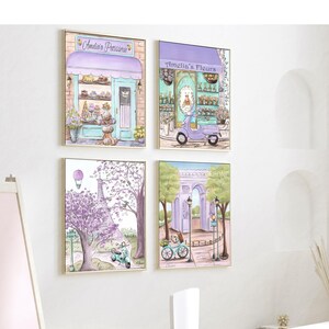 May include: Four framed illustrations of Parisian scenes. The top left image shows a pastel pink and blue storefront with the text "Amelie's Patisserie". The top right image shows a pastel pink and blue storefront with the text "Amelie's Fleurs". The bottom left image shows a purple Eiffel Tower with a hot air balloon in the sky. The bottom right image shows a purple archway with a bicycle in front of it.