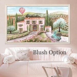 K&ouml;nnte beinhalten: Ein gerahmtes Aquarellbild, das eine rosafarbene Villa in einer h&uuml;geligen Landschaft mit Zypressen, einem rot-wei&szlig;en Hei&szlig;luftballon am Himmel und einem t&uuml;rkisfarbenen Roller auf einem Weg zeigt. Das Kunstwerk besticht durch sanfte Pastellt&ouml;ne.