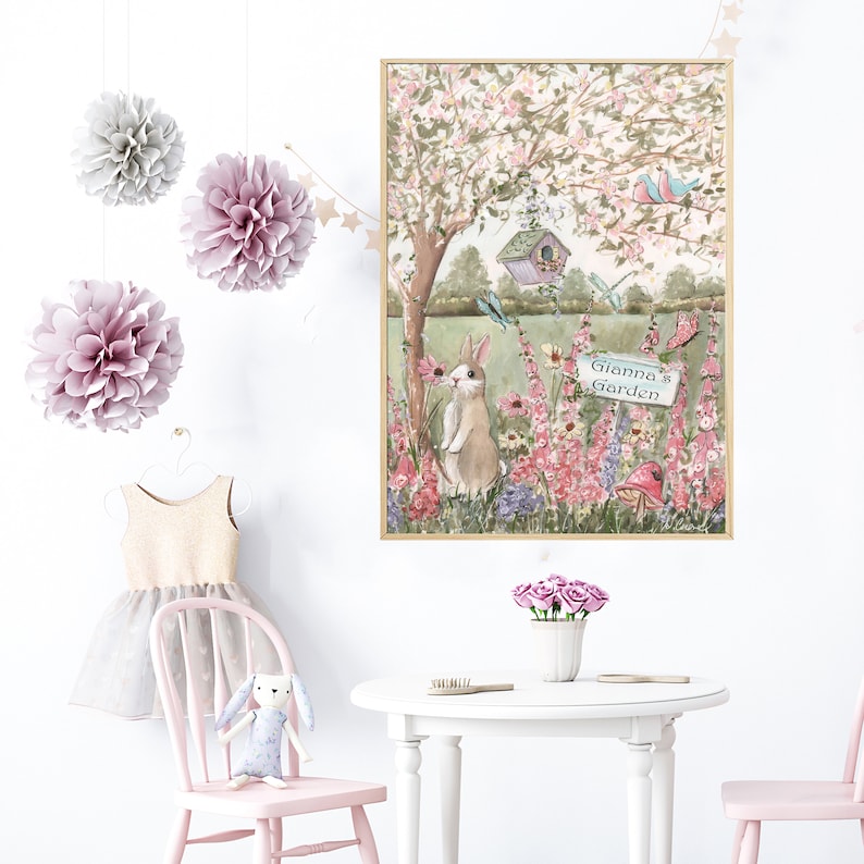 Puede incluir: Una ilustraci&oacute;n en tonos pastel rosa y verde de un conejo en un jard&iacute;n con un cartel que dice "Gianna's Garden". La ilustraci&oacute;n est&aacute; enmarcada en un marco dorado y colgada en una pared blanca.