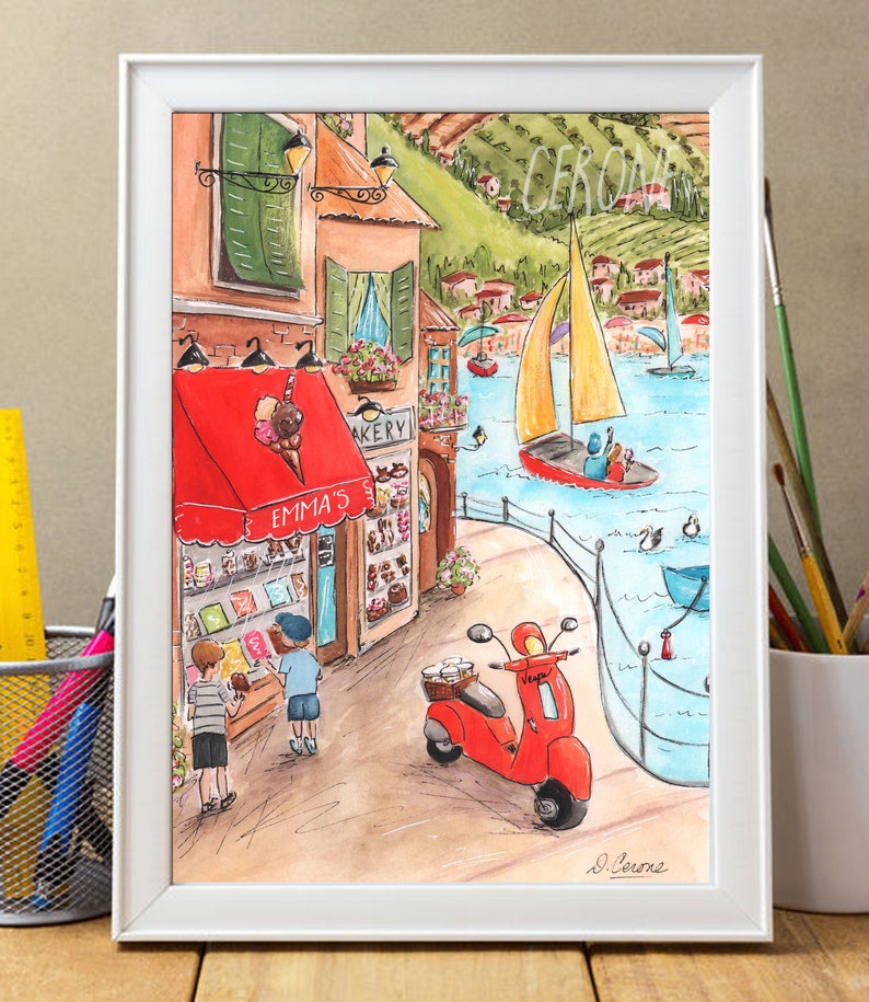 Op de afbeelding: Een aquarel schilderij van een schilderachtig Italiaans dorpje met een rode scooter, een bakkerij genaamd "Emma's" met een rode luifel en twee kinderen die naar het raam van de bakkerij kijken. Op de achtergrond vaart een zeilboot op een blauw meer.