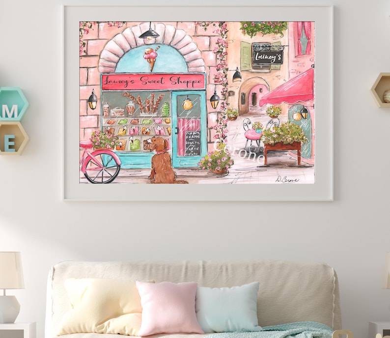 K&ouml;nnte beinhalten: Eine gerahmte Aquarellillustration eines Ladengesch&auml;fts namens Lainey's Sweet Shoppe mit t&uuml;rkisfarbenem Rahmen, rosafarbenen Ziegelw&auml;nden und einem Eist&uuml;ten-Schild. Ein brauner Hund sitzt drau&szlig;en bei einem rosa Fahrrad, mit Markise und Blumen.