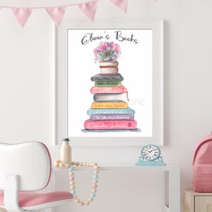 May include: Watercolor print of a stack of books with the text "Olivia's Books" and a floral arrangement on top. The book titles are visible. The artwork is framed in a white frame and displayed on a white wall.