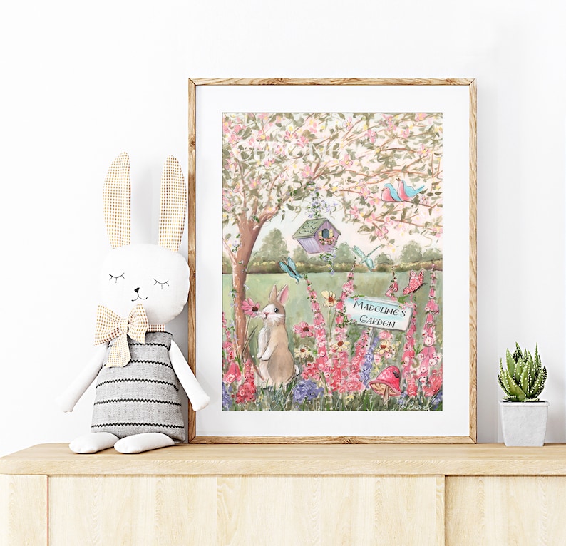 Puede incluir: Una pintura de acuarela de una escena de jard&iacute;n con un conejito, flores, una casita de p&aacute;jaros y un cartel que dice "El jard&iacute;n de Madeline".