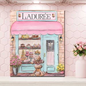 May include: A painting of a pink and blue storefront with the name "LADUR&Eacute;E" above the entrance. The storefront has a display of pastries in the window and a sign that says "PETITS MACARONS". A brown poodle is standing in front of the store looking at the pastries.