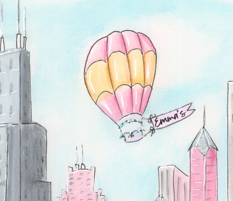May include: A pink and yellow hot air balloon with a banner that says "Emma's" is flying over a city skyline. The buildings are gray, pink, and white.