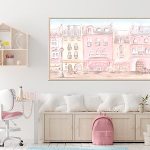 Op de afbeelding: Een aquarel schilderij van een rij pastelroze en gele gebouwen met een caf&eacute; in het midden. Het caf&eacute; heeft een bord met de tekst "Caf&eacute;". Er zitten mensen voor het caf&eacute; en er staat een fiets voor het gebouw.