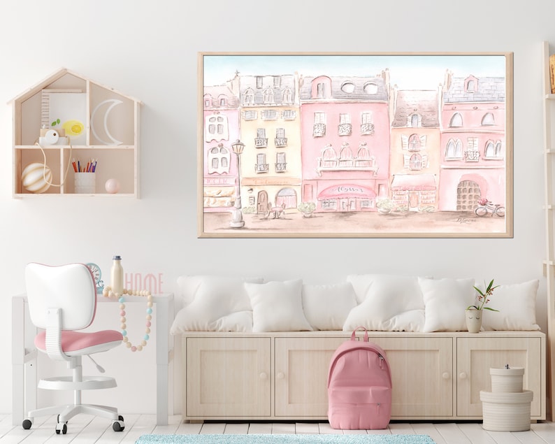 Op de afbeelding: Een aquarel schilderij van een rij pastelroze en gele gebouwen met een caf&eacute; in het midden. Het caf&eacute; heeft een bord met de tekst "Caf&eacute;". Er zitten mensen voor het caf&eacute; en er staat een fiets voor het gebouw.