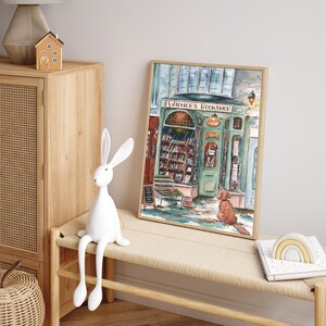 May include: A watercolor painting of a bookstore with a green awning and the words "Warner's Bookshop" above the entrance. A dog sits outside the shop, looking at the door. The painting is framed in a light wood frame.