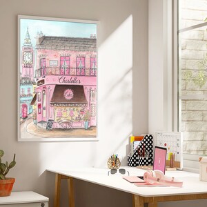 May include: A watercolor painting of a pink building with a brown awning that says "Charlotte's Cakes". The building is on a street with a red telephone booth and a clock tower in the background.