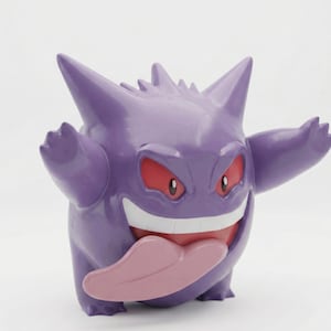 Op de afbeelding: Een paarse Gengar-figuur met een brede grijns, rode ogen en een roze tong. De figuur heeft stekelige kenmerken en uitgestrekte armen, wat een speels ontwerp laat zien. Een populair verzamelobject.