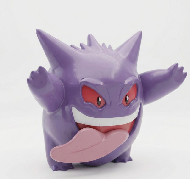 Op de afbeelding: Een paarse Gengar-figuur met een brede grijns, rode ogen en een roze tong. De figuur heeft stekelige kenmerken en uitgestrekte armen, wat een speels ontwerp laat zien. Een populair verzamelobject.