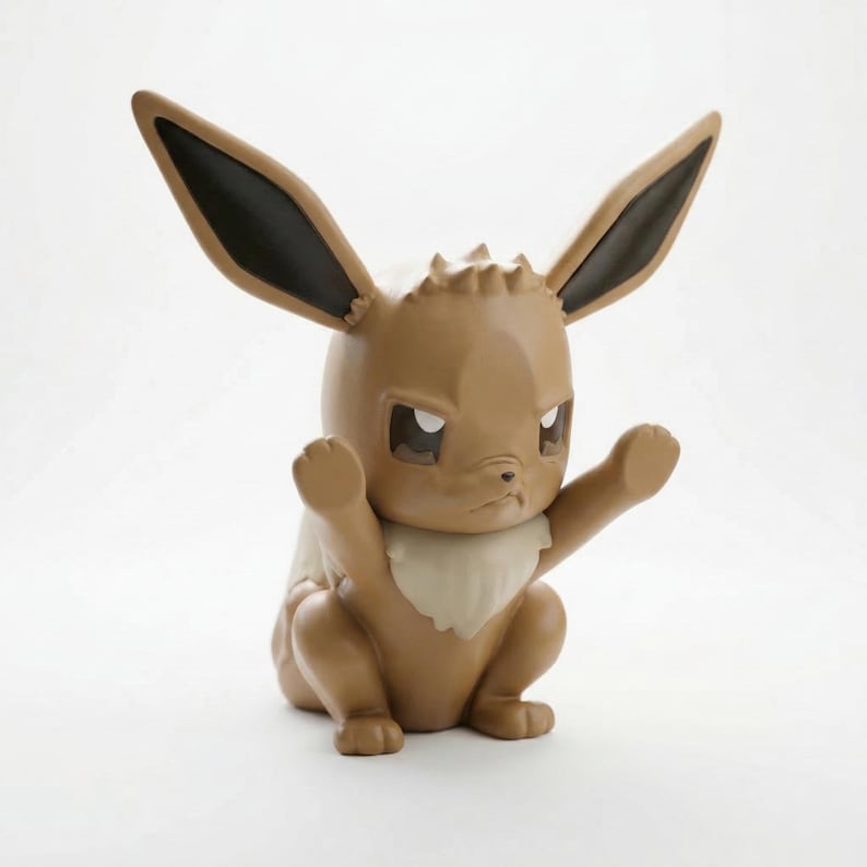 Op de afbeelding: Een bruin Eevee-beeldje met grote, puntige oren met zwarte punten en een cr&egrave;mekleurige kraag. Het beeldje staat in een hurkende pose met de armen omhoog. De ogen zijn donker en de uitdrukking is serieus.