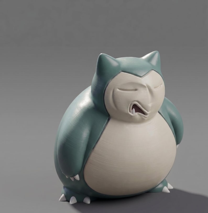 Op de afbeelding: Een beeldje van Snorlax, een groot Pok&eacute;mon, in blauwgroen en cr&egrave;me. De figuur wordt slapend afgebeeld, met gesloten ogen en een licht geopende mond. Het beeldje heeft een gladde, matte afwerking en is een verzamelobject.