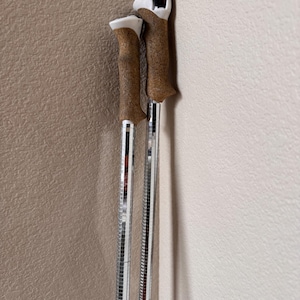 May include: A pair of ski poles with cork handles and mirrored shafts. The handles are brown with white and black details. The shafts are covered in small, reflective squares. The poles are against a corner wall.