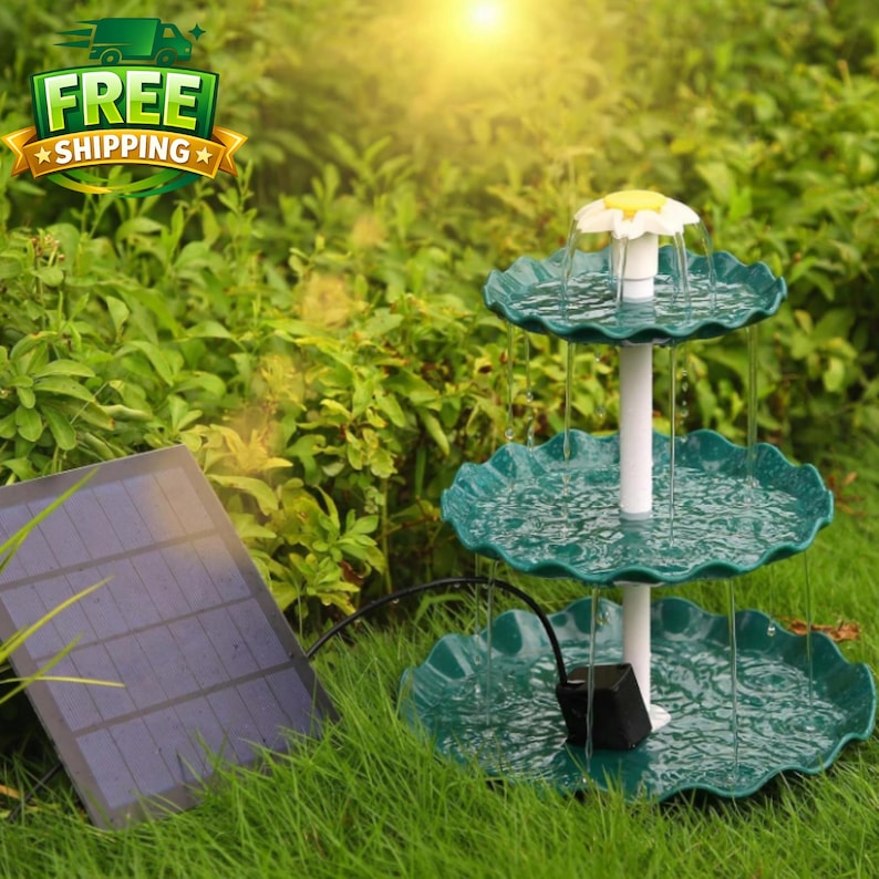 Pode incluir: Uma fonte de &aacute;gua exterior de tr&ecirc;s n&iacute;veis com um painel solar. A fonte tem um caule branco e bacias com bordas onduladas de cor verde-azulado. O topo da fonte &eacute; uma flor branca com um centro amarelo. A fonte est&aacute; numa &aacute;rea relvada.
