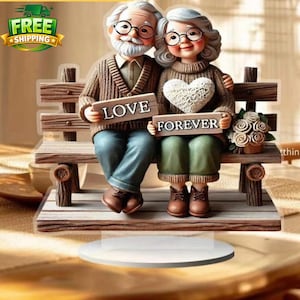 May include: A decorative figurine of an elderly couple sitting on a wooden bench. The man holds a sign that says "LOVE", and the woman holds a sign that says "FOREVER". The couple is wearing glasses and sweaters. A bouquet of flowers sits on the bench.