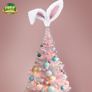 May include: A pink artificial Christmas tree decorated with pastel-colored ornaments and a silver spiral topper. The tree is topped with white bunny ears with pink inner ears. The image has a soft, dreamy aesthetic, perfect for Easter or spring decor.
