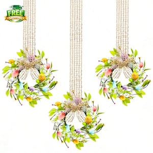 May include: Three Easter wreaths with colourful eggs, green leaves, and a burlap bow. Each wreath is suspended by a natural fibre cord. The wreaths are decorated with pastel-coloured eggs and small flowers, perfect for spring decor.