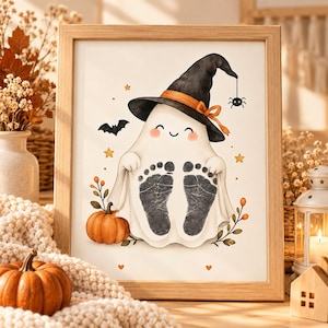May include: A framed print featuring a white ghost wearing a black witch hat with an orange ribbon. The ghost has two black baby footprints on its body, surrounded by a small orange pumpkin, a black bat, a spider, and yellow stars.