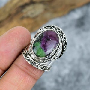 Könnte beinhalten: Ein Ring aus Sterlingsilber mit einem ovalen Rubin-Zoisit-Edelstein mit markanten magentafarbenen und grünen Einschlüssen. Das breite Band ist mit aufwendigen gedrehten Kordel- und Zickzack-Drahtmustern um den zentralen Stein verziert.