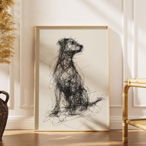 Puede incluir: Una impresión artística enmarcada con un dibujo lineal abstracto negro de un perro sentado. La obra de arte está sobre un fondo crema y enmarcada en un marco de madera clara. La impresión se exhibe en una habitación con un jarrón y un banco de bambú.