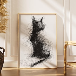 Könnte beinhalten: Gerahmter Kunstdruck mit einer schwarzen, abstrakten Katzenillustration. Die Katze ist in sitzender Position dargestellt, erstellt mit gekritzelten Linien vor einem weißen Hintergrund. Der Rahmen hat eine helle Holzfarbe und verleiht dem Kunstwerk Wärme.