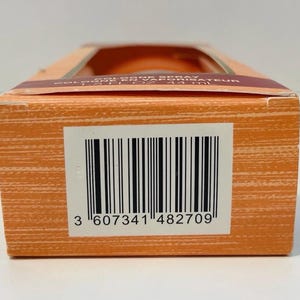 May include: Close-up of an orange rectangular box with a barcode and the number "3 607341 482709". The box has a window at the top, revealing the product inside. The box has a textured surface.