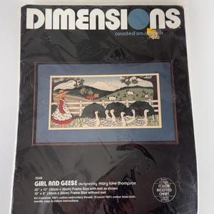 May include: A Dimensions counted cross stitch kit titled "GIRL AND GEESE" designed by Mary Lake Thompson. The kit includes embroidery thread, Aida cloth, and a needle. The finished size with mat is 20" x 12" (50cm x 30cm). The kit features a pastoral scene with a girl and geese.