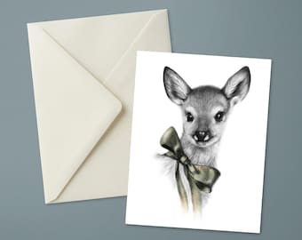 Peut inclure: Une carte de vœux présentant un dessin au crayon noir et blanc détaillé d'un jeune cerf aux grands yeux et aux oreilles pointues. Le cerf porte un nœud décoratif noué autour du cou. Une enveloppe blanc cassé est placée derrière la carte.