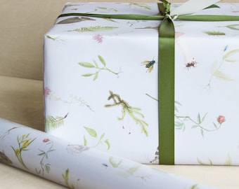 Peut inclure: Une boîte cadeau rectangulaire enveloppée dans du papier blanc avec un motif botanique de feuilles vertes, de petites fleurs et d'insectes, nouée avec un ruban de satin vert foncé et surmontée d'une étiquette blanche à bord doré.