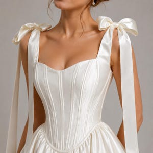 Elegant satin skater dress with corset waist, shoulder tie bows, and flowy mini skirt, romantic bridal aesthetic clothing.